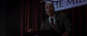 Movie still from “Donnie Darko” (2001), directed by Richard Kelly – A man standing at a podium speaking to a crowd; Close Up shot, Low angle
