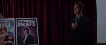 Movie still from “Donnie Darko” (2001), directed by Richard Kelly – A man standing in front of a poster of a movie; Medium shot, Over the shoulder angle