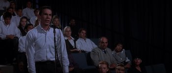 Movie still from “Donnie Darko” (2001), directed by Richard Kelly – A group of people sitting and standing in front of a microphone; Medium shot, Low angle