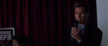 Movie still from “Donnie Darko” (2001), directed by Richard Kelly – A man holding a microphone while standing in front of a curtain; Close Up shot, Over the shoulder angle