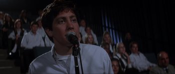Movie still from “Donnie Darko” (2001), directed by Richard Kelly – A man with a microphone in front of a group of people; Close Up shot, Low angle