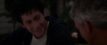 Movie still from “Donnie Darko” (2001), directed by Richard Kelly – A young man smiling while sitting next to another man; Close Up shot, Over the shoulder angle