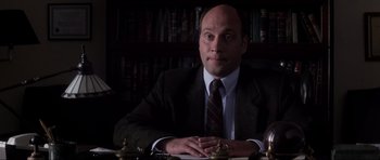 Movie still from “Donnie Darko” (2001), directed by Richard Kelly – A man sitting at a table in front of a book shelf; Close Up shot, Low angle