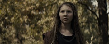 Movie still from “Don't Breathe 2” (2021), directed by Rodo Sayagues – A young girl with long hair standing in front of a tree; Close Up shot, Over the shoulder angle