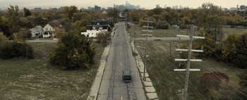 Movie still from “Don't Breathe 2” (2021), directed by Rodo Sayagues – A car driving down a street with a city skyline in the background; Extreme Wide shot, High angle