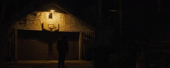 Movie still from “Don't Breathe 2” (2021), directed by Rodo Sayagues – A person standing in front of a garage at night; Wide shot, Low angle