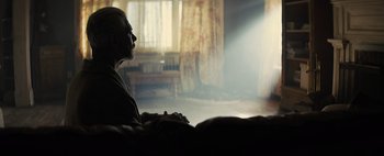 Movie still from “Don't Breathe 2” (2021), directed by Rodo Sayagues – A man sitting on a couch in a living room; Medium shot, Over the shoulder angle
