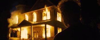 Movie still from “Don't Breathe 2” (2021), directed by Rodo Sayagues – A woman standing in front of a house on fire at night; Medium shot, Low angle