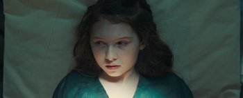 Movie still from “Don't Breathe 2” (2021), directed by Rodo Sayagues – A young girl is laying down in the dark; Close Up shot, High angle