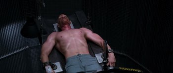 Movie still from “Doom” (2005), directed by Andrzej Bartkowiak – A shirtless man is sitting on a machine; Medium shot, High angle