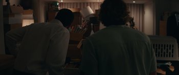 Movie still from “Down Low” (2023), directed by Rightor Doyle – Two people are looking at a book in a room; Medium shot, Over the shoulder angle