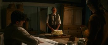Movie still from “Downton Abbey: A New Era” (2022), directed by Simon Curtis – An older man standing in front of a cake on top of a table; Medium shot, Over the shoulder angle