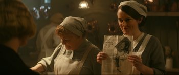 Movie still from “Downton Abbey: A New Era” (2022), directed by Simon Curtis – Two women dressed in period clothing looking at an old newspaper; Medium shot, Over the shoulder angle