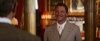 Movie still from “Downton Abbey: A New Era” (2022), directed by Simon Curtis – A man wearing a suit and tie smiling for the camera; Medium shot, Over the shoulder angle
