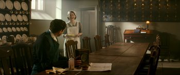 Movie still from “Downton Abbey: A New Era” (2022), directed by Simon Curtis – A woman standing at a dining room table holding a plate; Medium shot, Over the shoulder angle