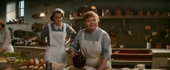Movie still from “Downton Abbey: A New Era” (2022), directed by Simon Curtis – Two women in aprons in a kitchen preparing food; Medium shot, Low angle
