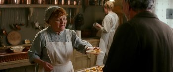 Movie still from “Downton Abbey: A New Era” (2022), directed by Simon Curtis – An older woman in an old - fashioned kitchen holding a plate of food; Medium shot, Over the shoulder angle