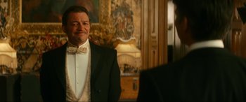 Movie still from “Downton Abbey: A New Era” (2022), directed by Simon Curtis – A man in a tuxedo standing in front of a painting; Medium shot, Over the shoulder angle