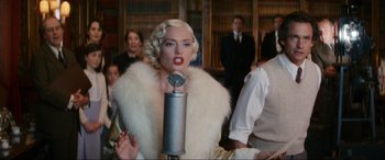 Movie still from “Downton Abbey: A New Era” (2022), directed by Simon Curtis – A woman in a white fur coat is holding a microphone in her hand; Medium shot, Low angle