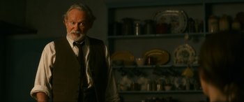 Movie still from “Downton Abbey: A New Era” (2022), directed by Simon Curtis – An older man standing in front of a shelf of dishes; Medium shot, Over the shoulder angle