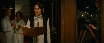 Movie still from “Downton Abbey: A New Era” (2022), directed by Simon Curtis – A woman standing in front of a microphone in a room; Medium shot, Low angle