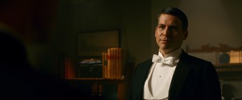 Movie still from “Downton Abbey: A New Era” (2022), directed by Simon Curtis – A man in a tuxedo standing in front of a bookshelf; Medium shot, Over the shoulder angle