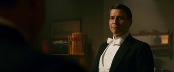 Movie still from “Downton Abbey: A New Era” (2022), directed by Simon Curtis – A man in a tuxedo standing next to a bookshelf; Medium shot, Low angle