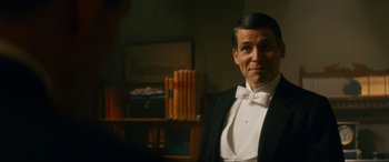 Movie still from “Downton Abbey: A New Era” (2022), directed by Simon Curtis – A man in a tuxedo standing next to a bookshelf; Medium shot, Over the shoulder angle