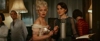 Movie still from “Downton Abbey: A New Era” (2022), directed by Simon Curtis – Two women are posing for a picture while one of them is holding a microphone; Medium shot, Over the shoulder angle