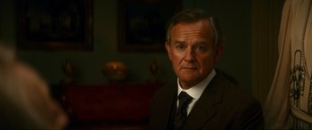Movie still from “Downton Abbey: A New Era” (2022), directed by Simon Curtis – An older man wearing a suit and tie in a room; Close Up shot, Low angle