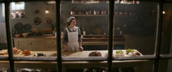 Movie still from “Downton Abbey: A New Era” (2022), directed by Simon Curtis – A woman standing at a counter in a kitchen; Medium shot, High angle