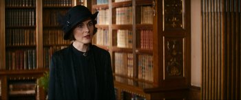 Movie still from “Downton Abbey: A New Era” (2022), directed by Simon Curtis – A woman wearing a black hat standing in front of a book case; Medium shot, Over the shoulder angle