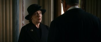 Movie still from “Downton Abbey: A New Era” (2022), directed by Simon Curtis – An older woman wearing a black hat looking at a man in a suit; Close Up shot, Over the shoulder angle