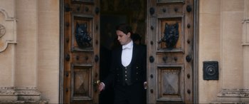Movie still from “Downton Abbey: A New Era” (2022), directed by Simon Curtis – A man in a tuxedo standing in front of a door; Medium shot, Low angle