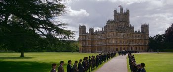 Movie still from “Downton Abbey: A New Era” (2022), directed by Simon Curtis – A long line of men in suits and hats in front of a large building; Extreme Wide shot, Low angle