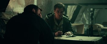 Movie still from “12 Strong” (2018), directed by Nicolai Fuglsig – A man sitting at a table with another man in front of him; Medium shot, Over the shoulder angle