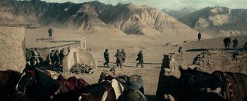Movie still from “12 Strong” (2018), directed by Nicolai Fuglsig – A group of men walking across a dirt field; Extreme Wide shot, High angle
