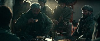 Movie still from “12 Strong” (2018), directed by Nicolai Fuglsig – A group of men sitting around a table eating food; Medium shot, High angle