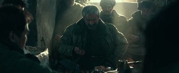 Movie still from “12 Strong” (2018), directed by Nicolai Fuglsig – An older man sitting at a table with a plate of food; Medium shot, Over the shoulder angle