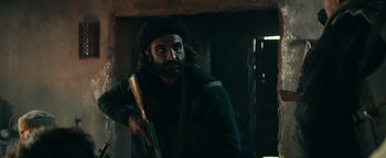 Movie still from “12 Strong” (2018), directed by Nicolai Fuglsig – A man with a beard holding a rifle in a room; Medium shot, Over the shoulder angle