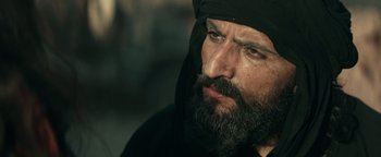 Movie still from “12 Strong” (2018), directed by Nicolai Fuglsig – A man with a beard wearing a head covering; Close Up shot, Over the shoulder angle