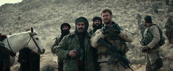 Movie still from “12 Strong” (2018), directed by Nicolai Fuglsig – A group of men standing next to each other holding guns; Medium shot, Over the shoulder angle