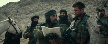 Movie still from “12 Strong” (2018), directed by Nicolai Fuglsig – A group of men standing next to each other holding papers; Medium shot, Over the shoulder angle