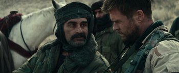 Movie still from “12 Strong” (2018), directed by Nicolai Fuglsig – A man in a fur hat and a scarf; Close Up shot, Over the shoulder angle