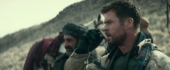 Movie still from “12 Strong” (2018), directed by Nicolai Fuglsig – Two men are standing in the desert while one of them holds his hand up to his ear; Close Up shot, Over the shoulder angle