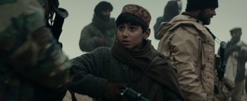 Movie still from “12 Strong” (2018), directed by Nicolai Fuglsig – A young man holding a gun while standing next to other men; Medium shot, Over the shoulder angle