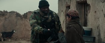 Movie still from “12 Strong” (2018), directed by Nicolai Fuglsig – A man in a camouflage jacket is holding a gun and talking to a woman; Medium shot, Over the shoulder angle