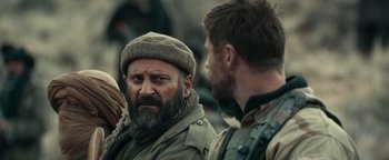 Movie still from “12 Strong” (2018), directed by Nicolai Fuglsig – A man with a beard wearing a hat talking to another man; Close Up shot, Over the shoulder angle