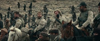 Movie still from “12 Strong” (2018), directed by Nicolai Fuglsig – A group of men standing next to each other on a field; Medium shot, Over the shoulder angle