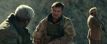Movie still from “12 Strong” (2018), directed by Nicolai Fuglsig – A man in a military uniform sitting on the ground; Medium shot, Over the shoulder angle